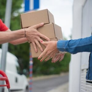 Hands exchanging cardboard boxes during an outdoor delivery scene.